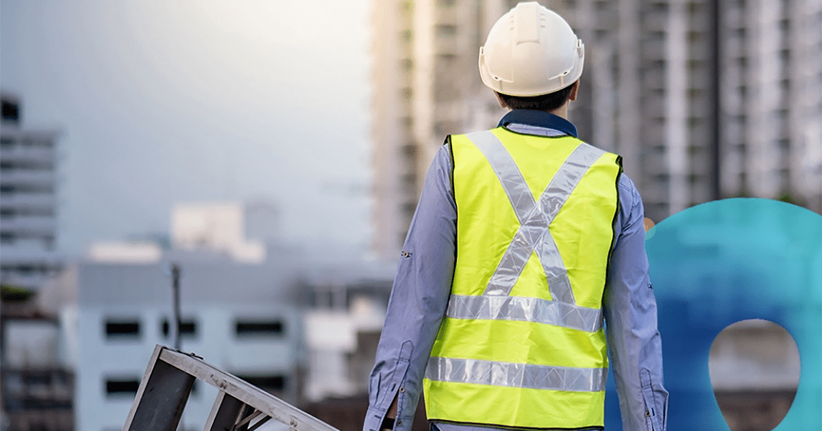 A person in a safety vest and hardhat carrying a ladder